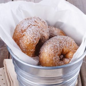 Sugar powdered cinnamon doughnuts in a metal bucket on rustic wooden background close up