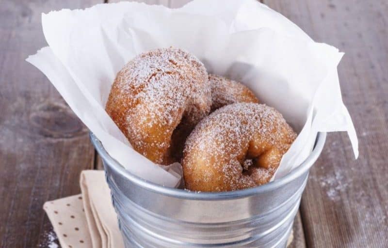 Sugar powdered cinnamon doughnuts in a metal bucket on rustic wooden background close up